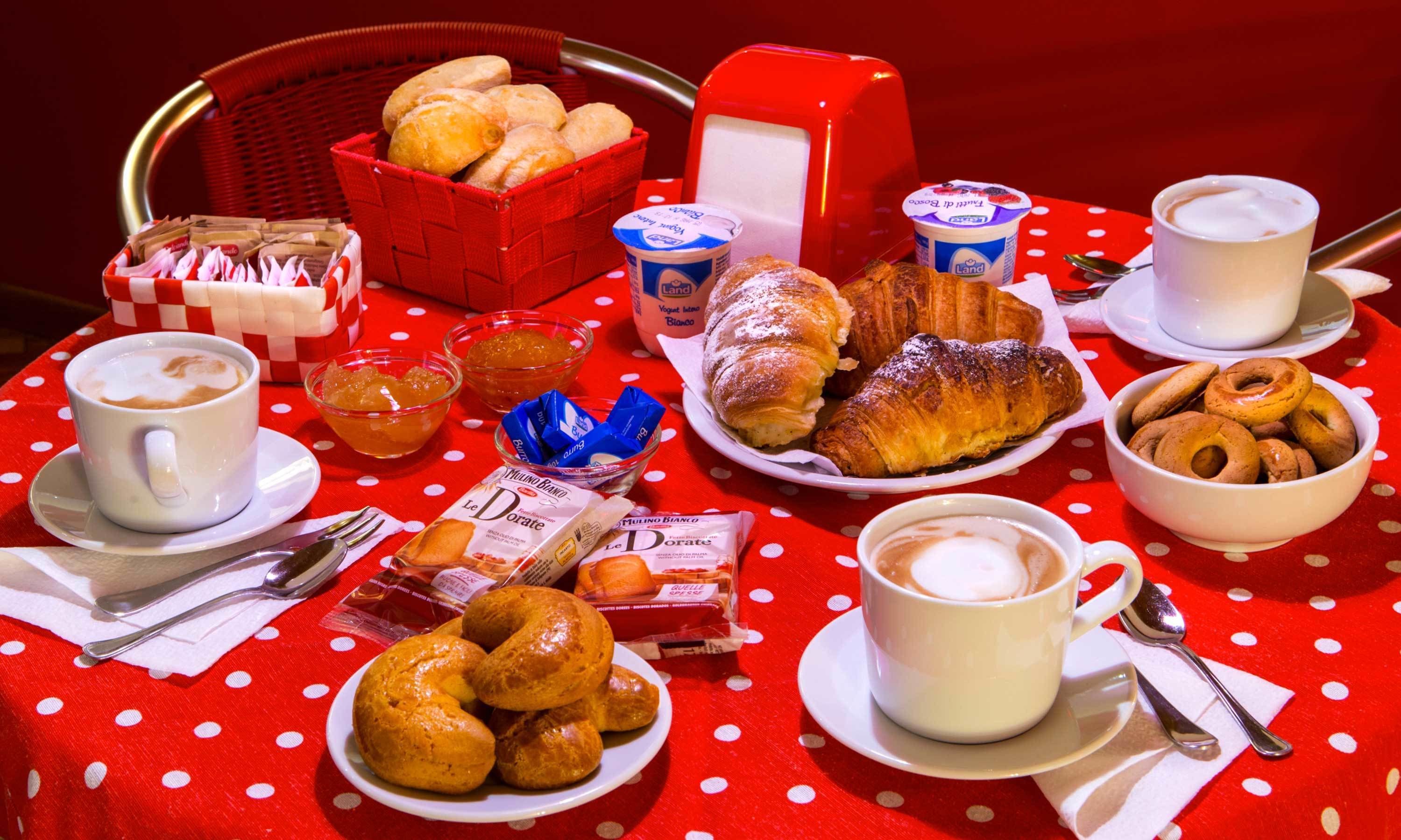 A breakfast setting with croissants, pastries, coffee, and a basket of bread.