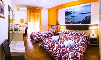 Quarto de hotel com duas camas, uma escrivaninha, uma cadeira, televisão e uma janela grande com vista para o litoral.