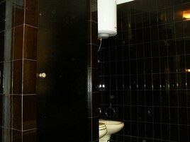 Ein Badezimmer mit schwarzen Fliesenwänden, einer weißen Toilette und einem weißen Gerät an der Decke.