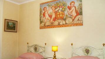 A bedroom with two beds, a nightstand with a lamp, and a painting of cherubs on the wall.