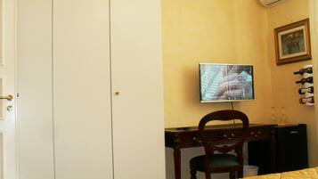 Habitación de hotel con cama, escritorio con silla, televisor y una estantería para vinos en la pared.