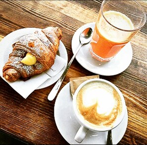 A croissant with powdered sugar and a lemon slice on a plate, a glass of orange juice, and a cup of coffee with latte art on a wooden table. - I 13 Cavalieri Guest House (Barletta)