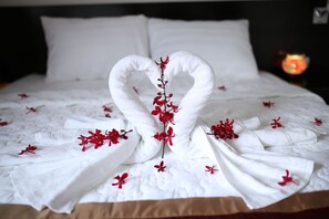 Una cama bien hecha con una toalla dispuesta en forma de corazón, con flores rojas.