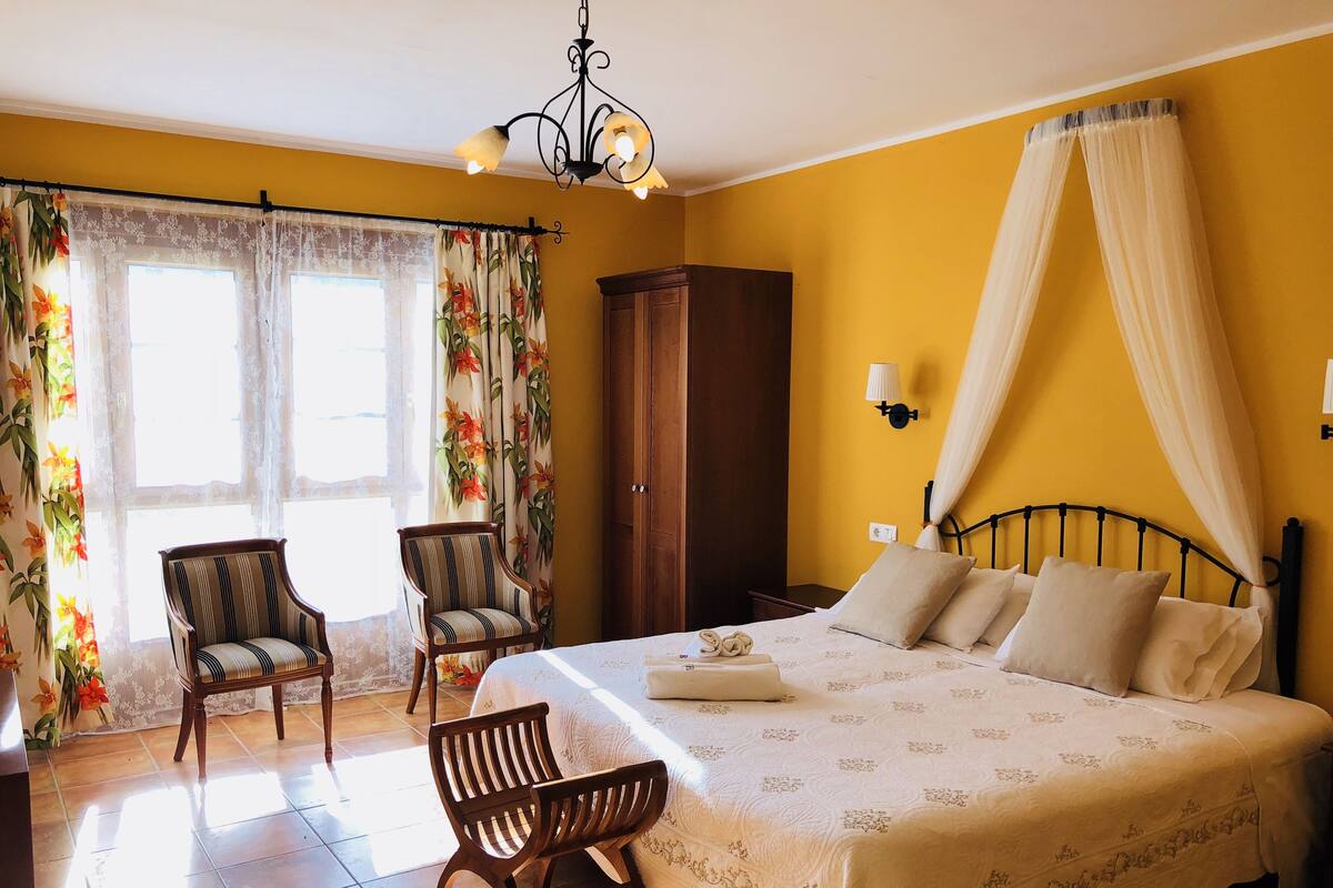 A bedroom with a bed, two chairs, a wardrobe, and a window with curtains.