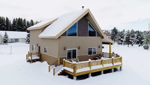 Une cabane moderne dotée d’une grande terrasse, entourée d’arbres couverts de neige.