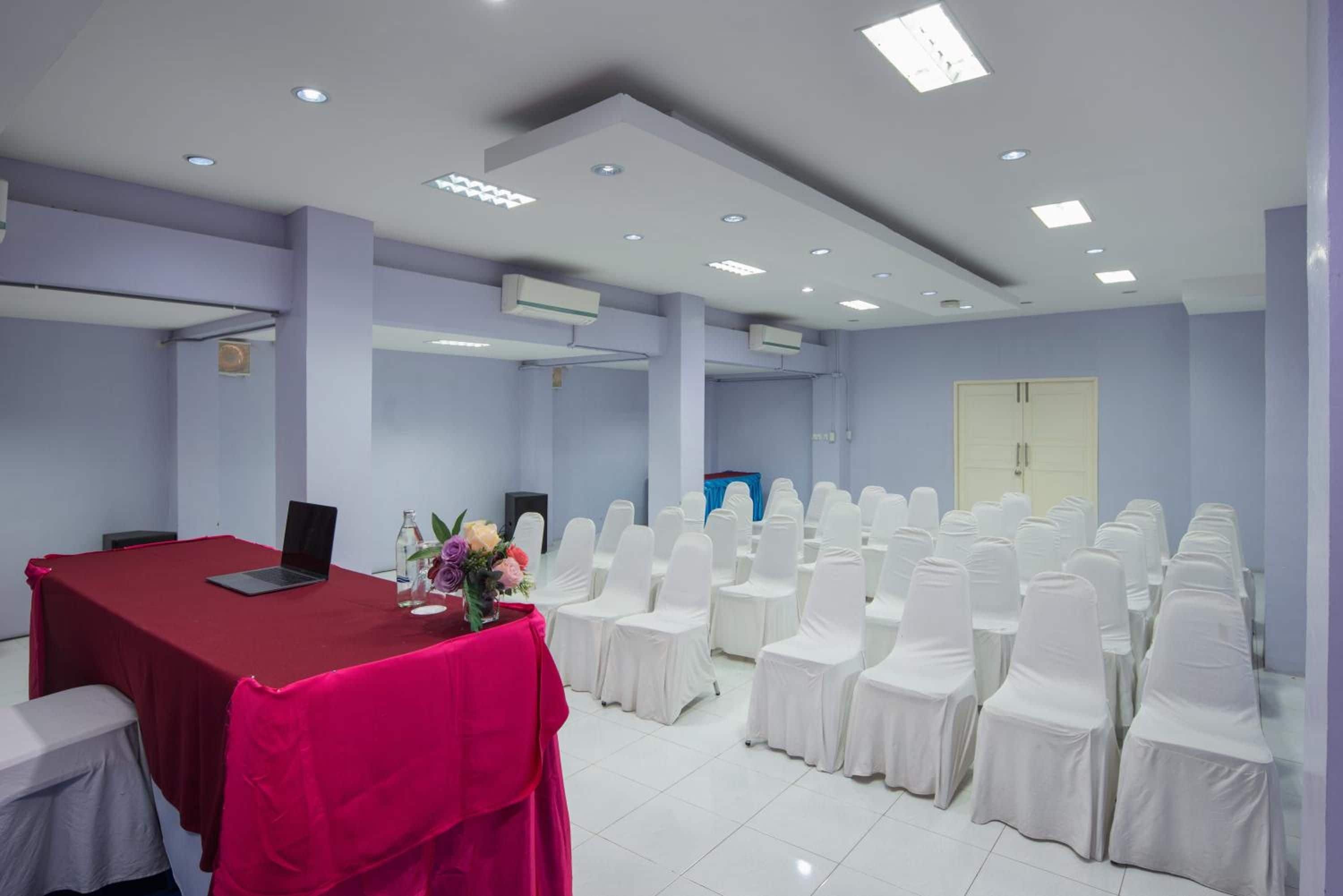 A conference room with a red table, white chairs, and a laptop.