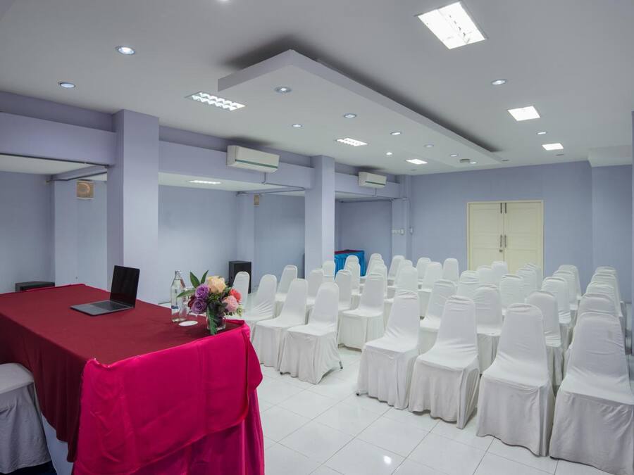 Un salón de conferencias con una mesa roja, sillas blancas y una computadora portátil.
