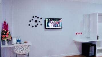 A modern living room with a flat-screen TV mounted on the wall, a white console table with a vase of flowers, a white chair, and a black speaker.