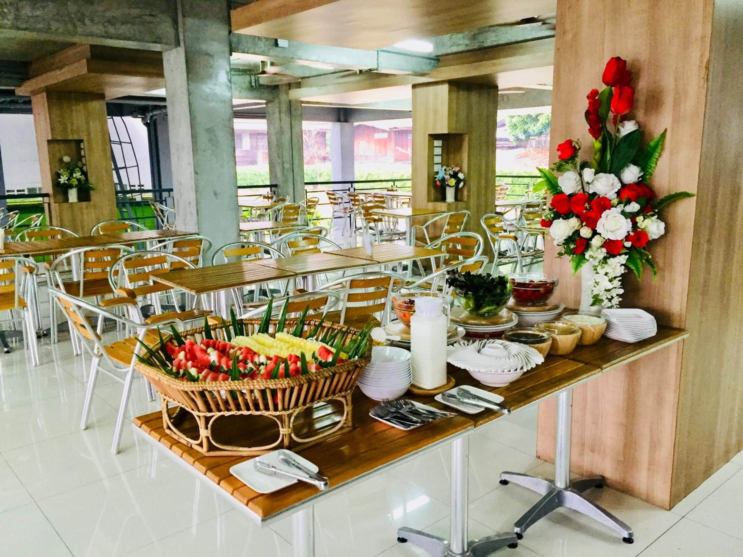 Un comedor con mesas dispuestas para una comida, destacando una cesta de frutas en el centro y un arreglo floral.