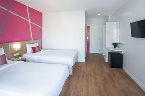 A hotel room with two beds, a TV, a mirror, and a small desk with a plant.