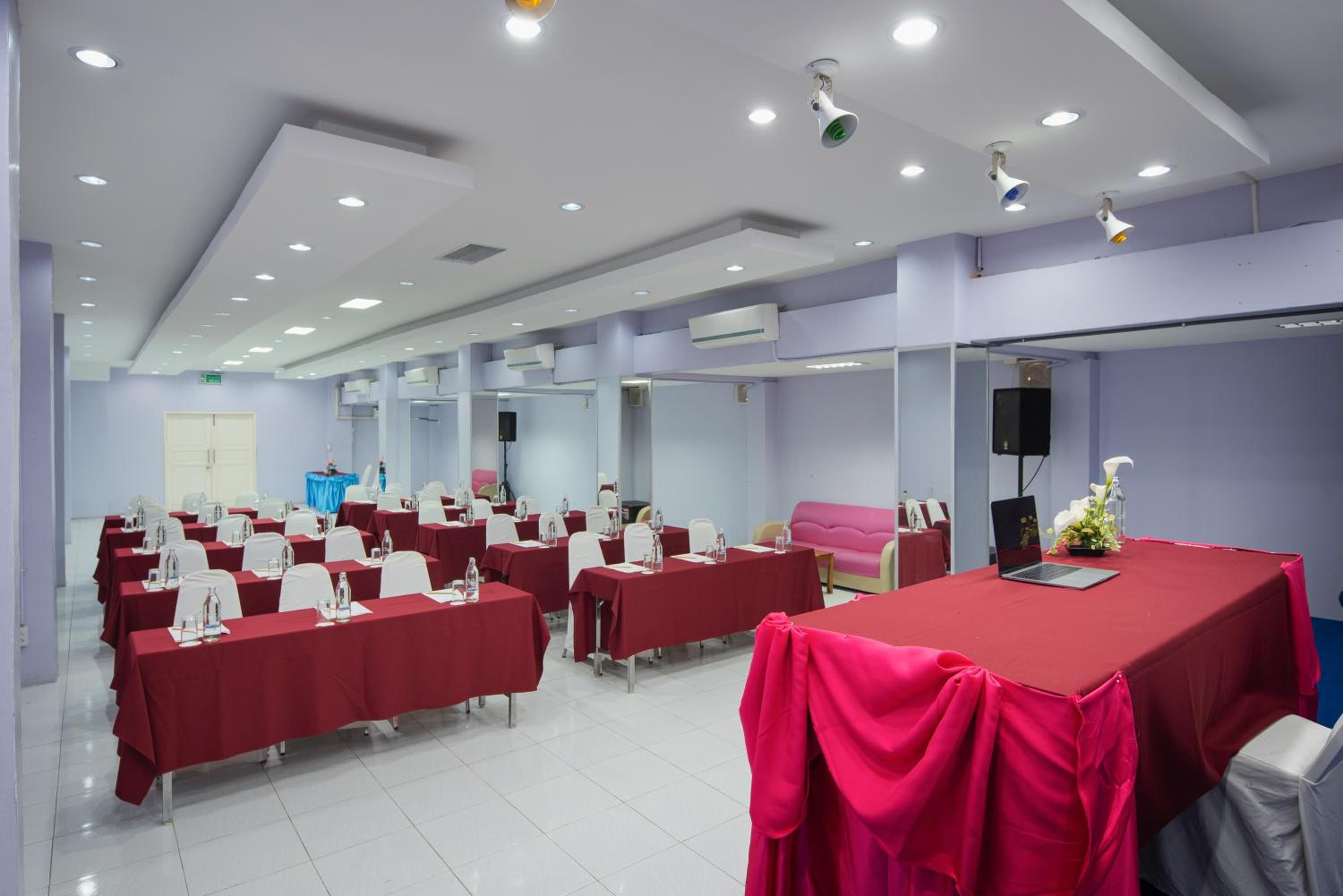 Une salle de conférence équipée de plusieurs tables, de chaises et d’une grande table rouge sur laquelle se trouve un ordinateur portable.