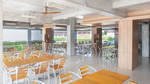 Un vaste espace de restauration intérieur, doté de nombreuses tables et chaises, de piliers en béton et de ventilateurs de plafond.