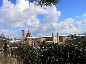 A historic building with a prominent clock tower and a dome, surrounded by snow-covered hills and trees. - B&B Aquilone (Urbino)
