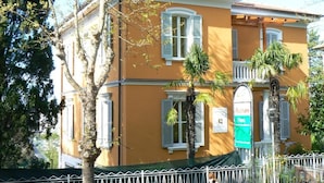 Un edificio de dos pisos con fachada amarilla, contraventanas blancas y toldo verde.