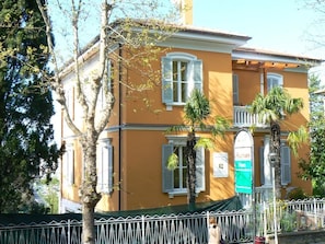 A two-story building with a yellow facade, white shutters, and a green awning. - B&B Aquilone (Urbino)