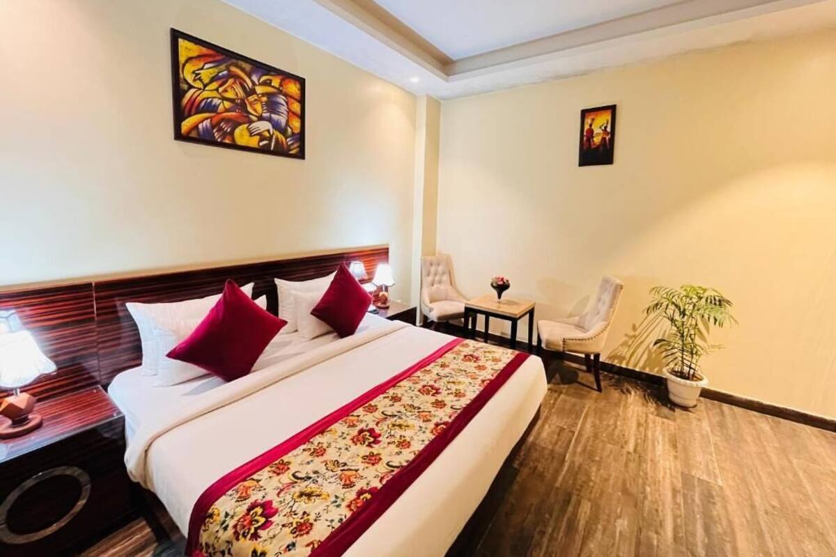 Una habitación de hotel con una cama grande, dos sillones, una mesita y una planta en maceta.