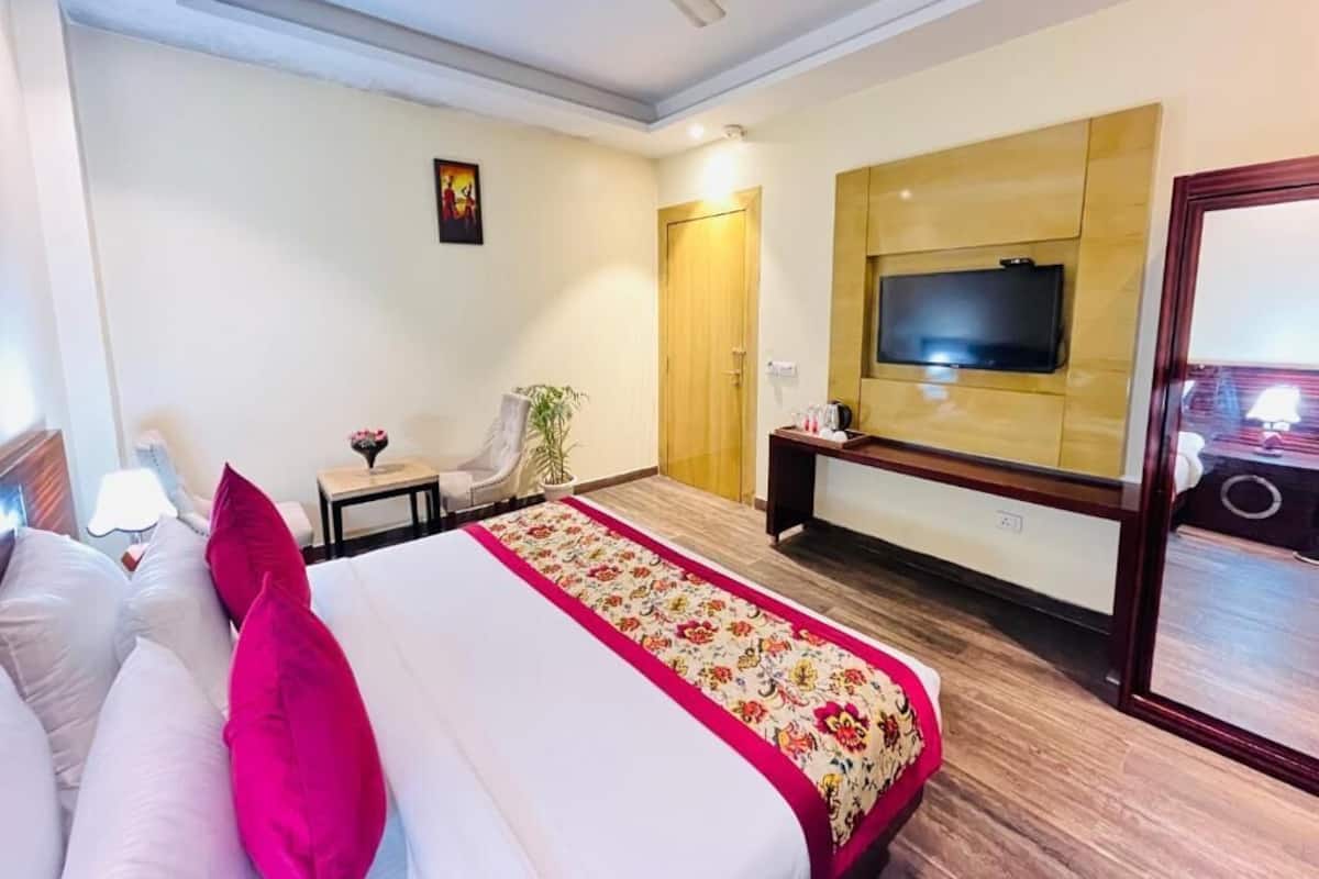 Habitación de hotel con una cama, un televisor en la pared, un ventilador de techo y piso de madera.