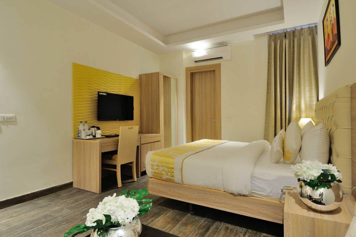 Habitación de hotel con cama, escritorio con silla, televisor y ventana con cortinas.