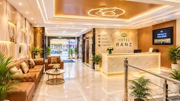 A hotel lobby with a reception desk, a sofa, a coffee table, and potted plants.