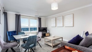 A modern living room with a dining area, a sofa, a coffee table, and a TV. - Carrick Retreat - Donnini Apartments (Ayr)