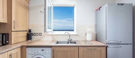 A modern kitchen with wooden cabinets, a built-in dishwasher, a stainless steel sink, and a refrigerator.