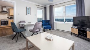 A modern living room with a dining area, a TV, and a view of the sea. - Carrick Retreat - Donnini Apartments (Ayr)