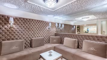 A luxurious living room with a tufted beige sofa, a small square coffee table, and a chandelier.