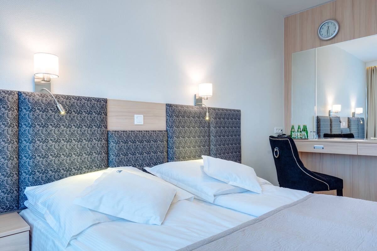 Een hotelkamer met een bed, twee wandlampen, een bureau met een spiegel en een stoel.