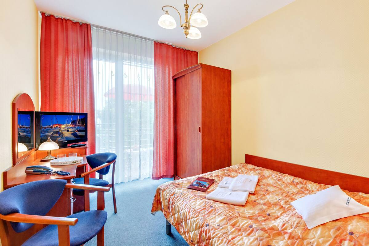 Een hotelkamer met een bed, een bureau met stoel, een televisie en een raam met gordijnen.