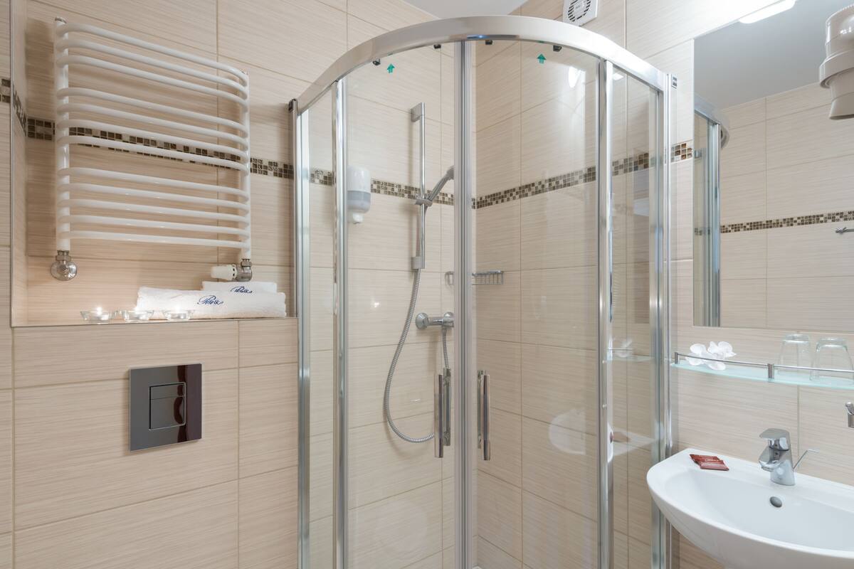 Een moderne badkamer met een douchecabine van glas, een witte wastafel en een handdoekhouder.
