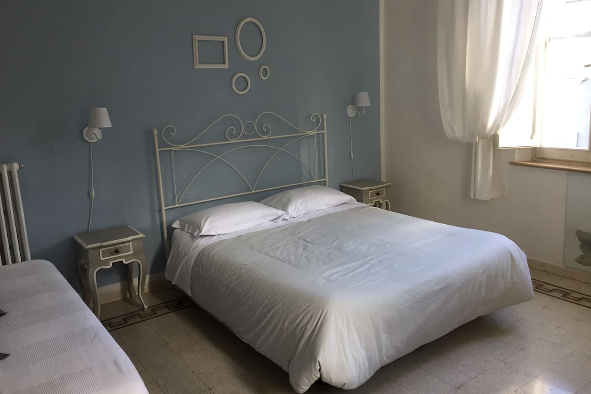 A neatly made bed in a room with a blue wall, two bedside tables with lamps, and a radiator.