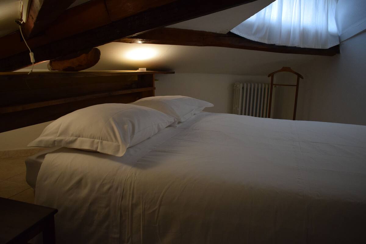 A bedroom with a wooden headboard, a bed with white linens, and a radiator in the background.