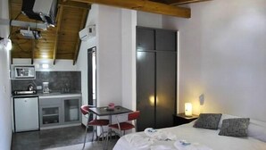 A compact hotel room with a kitchenette, a bed with pillows, and a bedside table with a lamp. - El Horreo Apart (Villa Gesell)