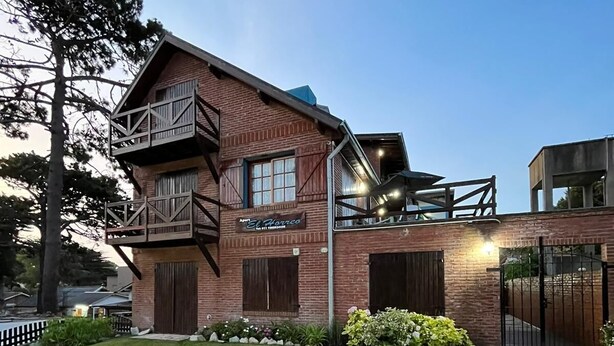 A two-story building with a sign reading "El Horneo." It features a brick facade, a balcony, and a stone pathway leading to the entrance. - El Horreo Apart (Villa Gesell)
