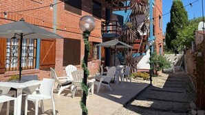 A courtyard with outdoor seating, a staircase, and a building with a brick facade and blue accents. - El Horreo Apart (Villa Gesell)
