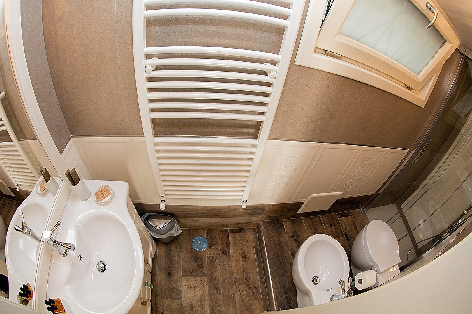 A bathroom with two sinks, a toilet, and a bidet. There is a towel rack and a window above the toilet.