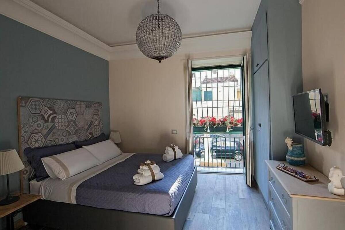 Un dormitorio con cama, un candelabro, un televisor y un balcón lleno de flores.