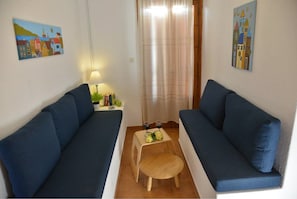 Ein kleiner, gemütlicher Raum mit zwei blauen Sofas, einem Holztisch mit Früchten und Getränken sowie einem Vorhang.