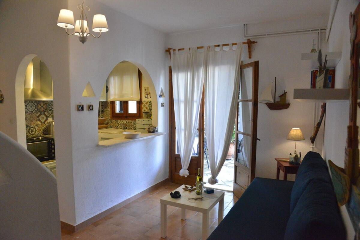 Una sala de estar con un sofá, una mesita con una botella, un espejo y una ventana con cortinas.