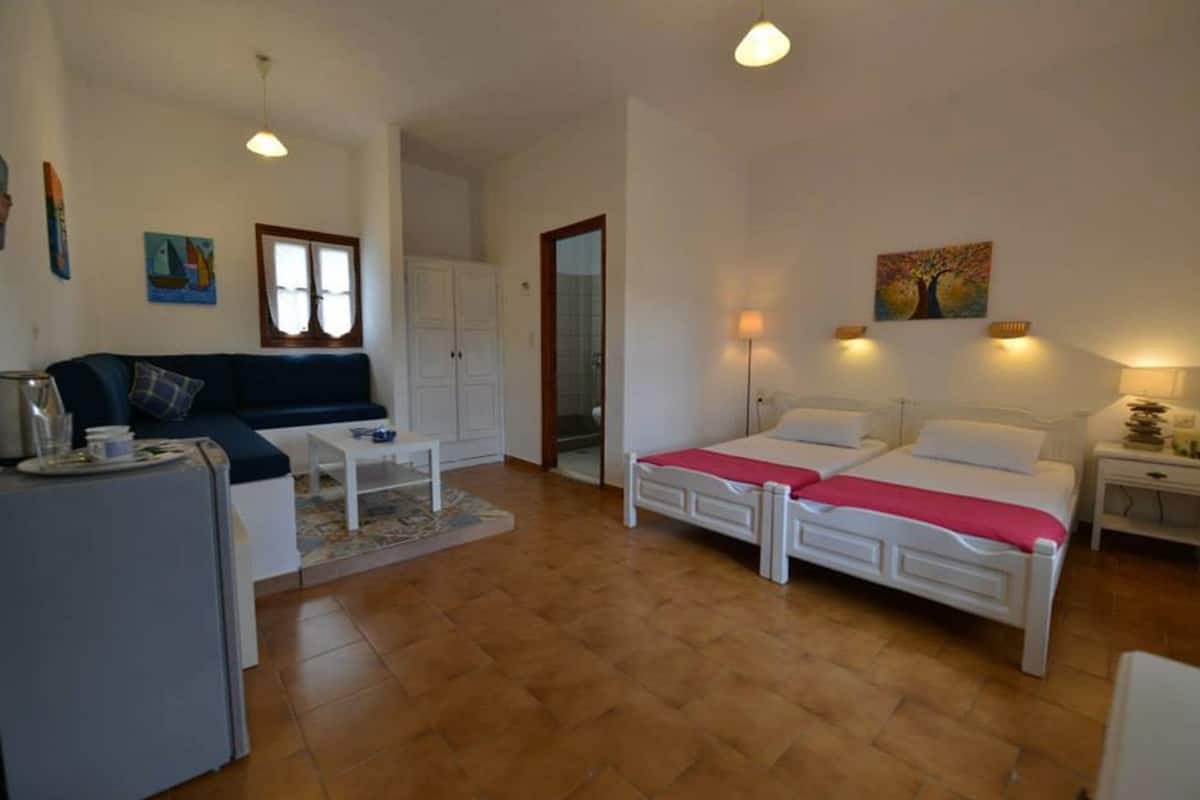 Una habitación compacta con una cama, un sofá, una mesita y un armario.