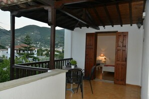 A balcony with a wooden railing, a table with chairs, and a view of a town and mountains in the background. - Anofli Accommodation (Skopelos)