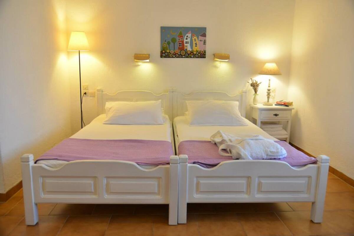 Una cama doble con estructura blanca, dos mesitas de noche con lámparas y un cuadro en la pared.