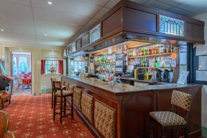 Zona de bar con mostrador, taburetes y una variedad de botellas y vasos.