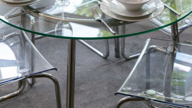 A round glass table set with white bowls and wine glasses, surrounded by metal chairs. - Elms Way - Donnini Apartments (Ayr)