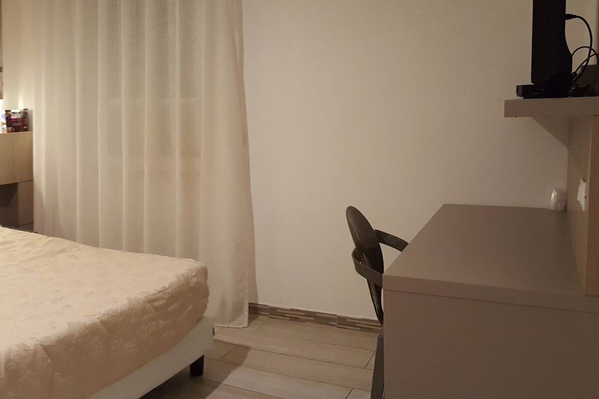 A hotel room with a bed, bedside table, and a mirror.