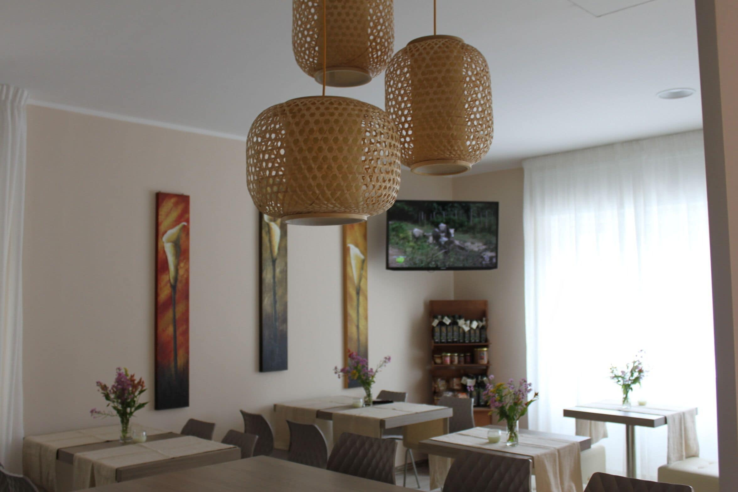 A dining area with tables, chairs, hanging woven light fixtures, a television, and artwork on the walls.