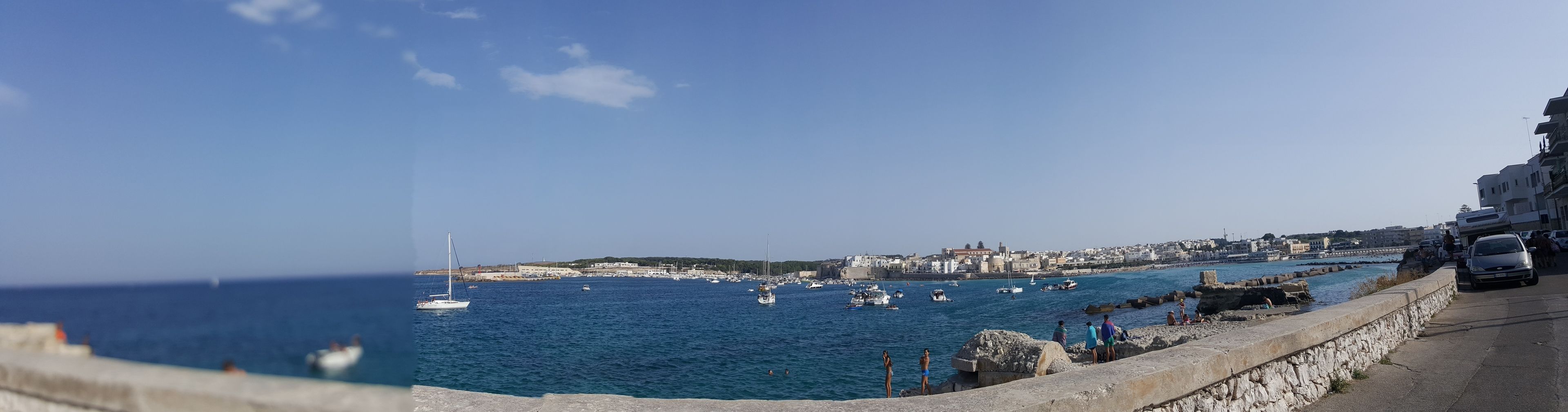 A coastal town with a stone wall, boats, and a clear blue sky.