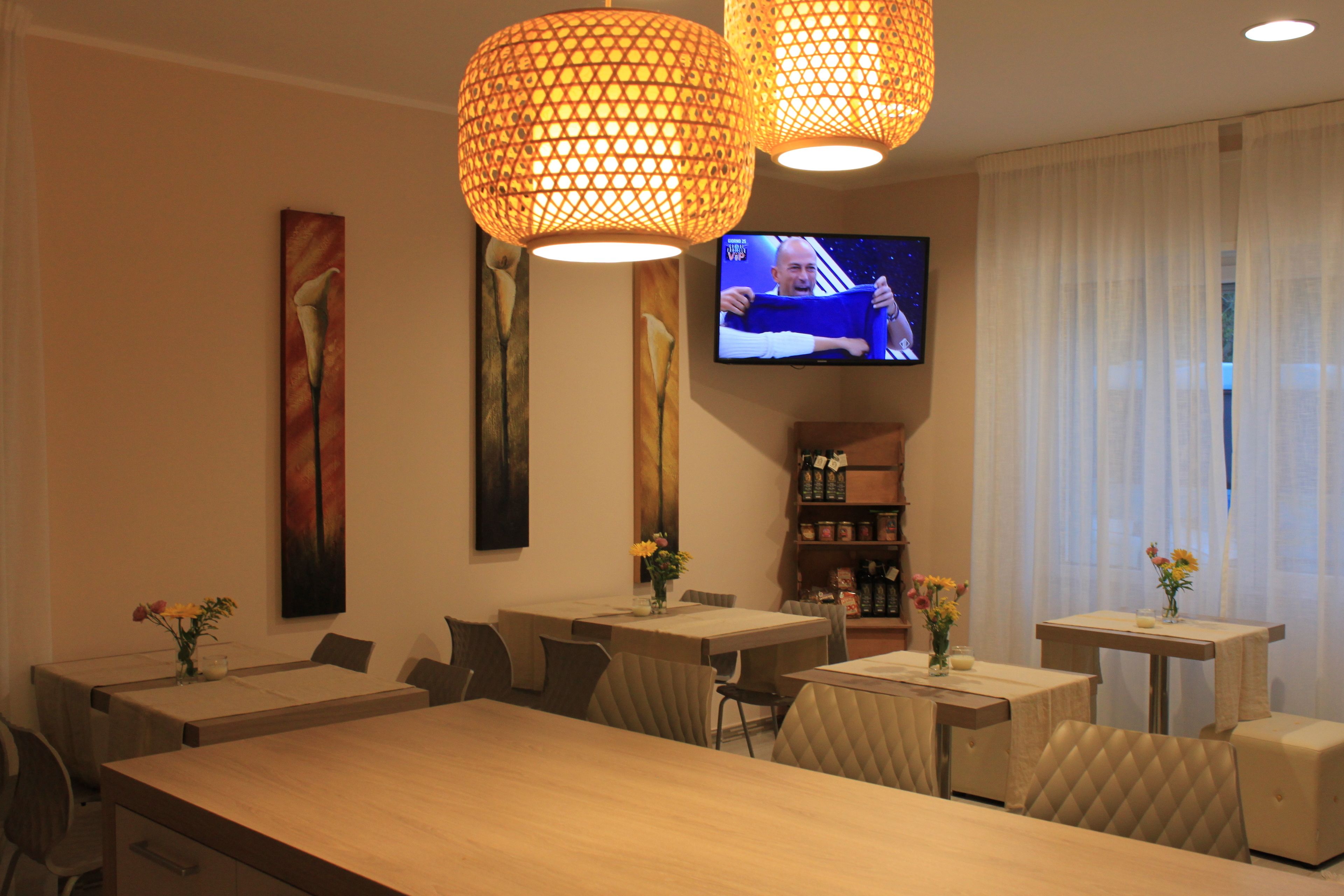 Comedor de hotel con varias mesas y sillas, un televisor montado en la pared y lámparas decorativas.