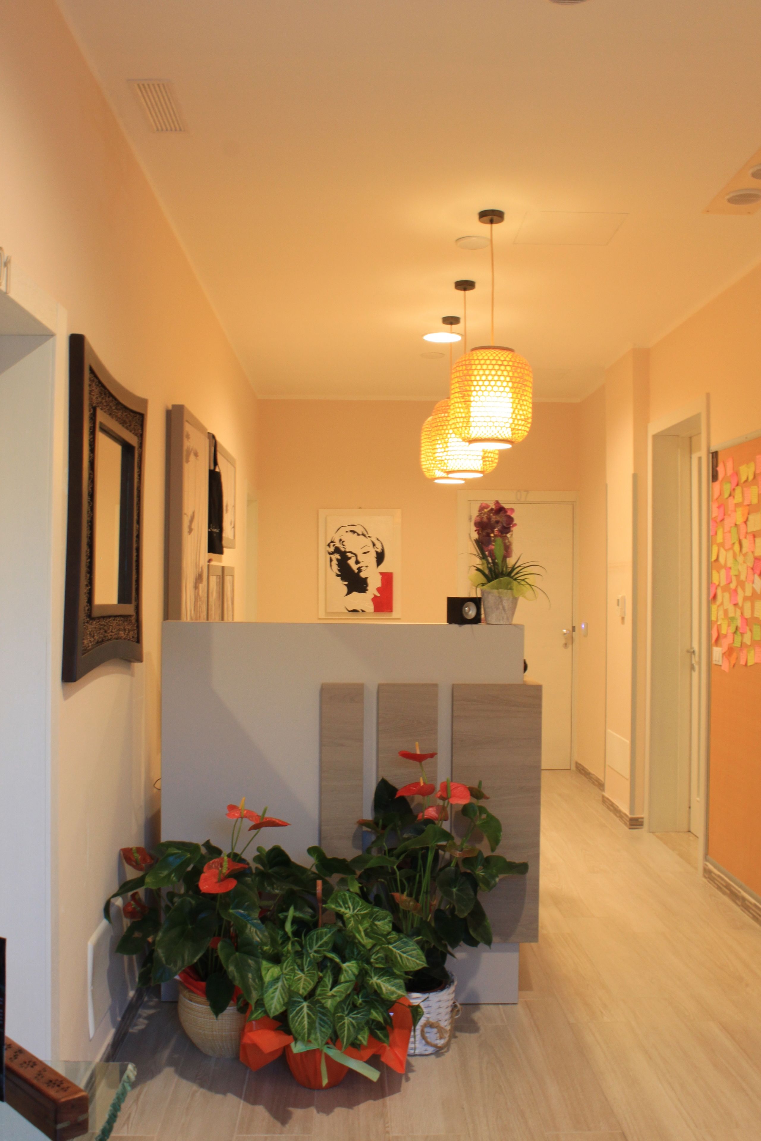 A hallway with a reception desk, potted plants, artwork, and a hanging light fixture.