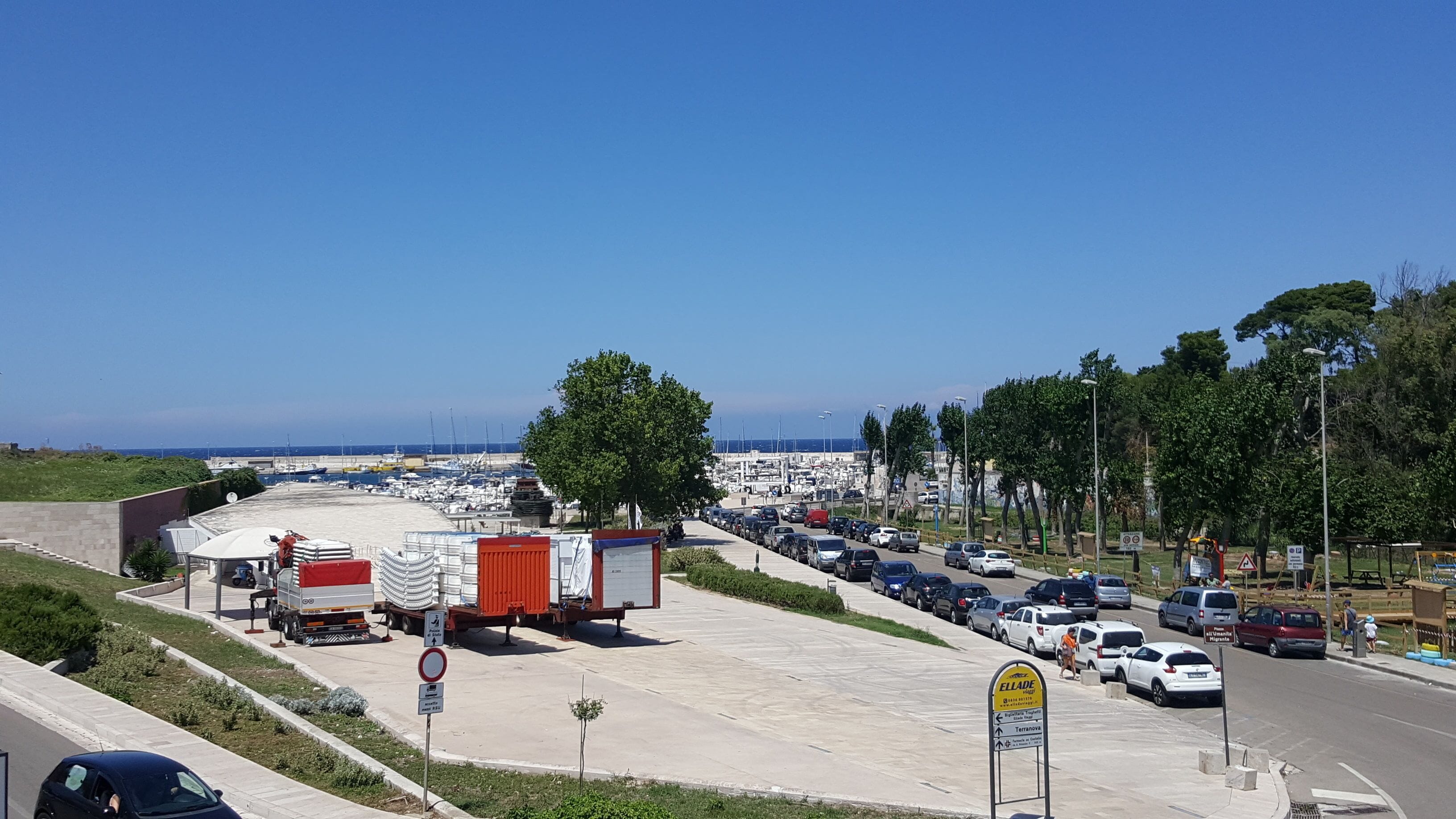 A parking lot with a view of a marina and boats in the background.